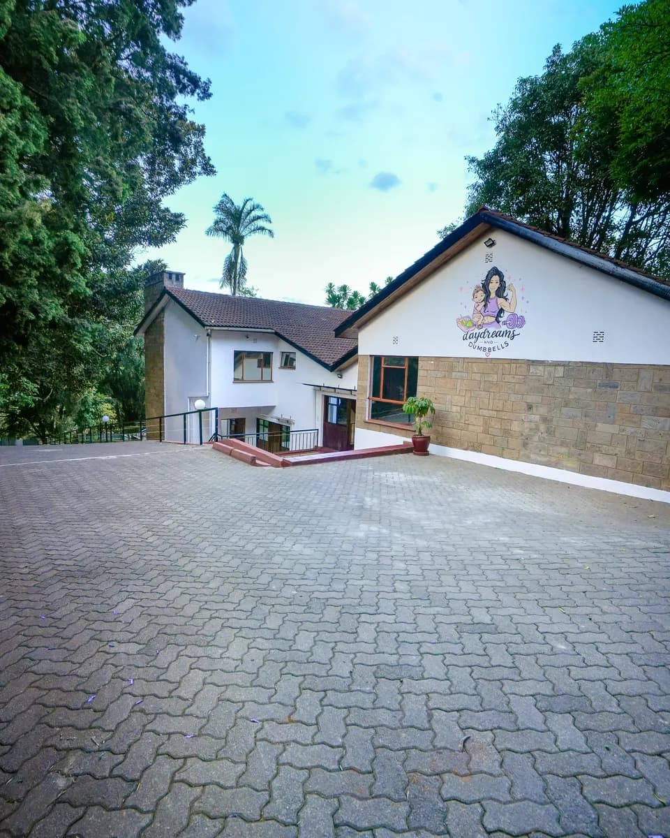 The Daydreams & Dumbbells building, a white house with the logo on its gable, set among tall trees