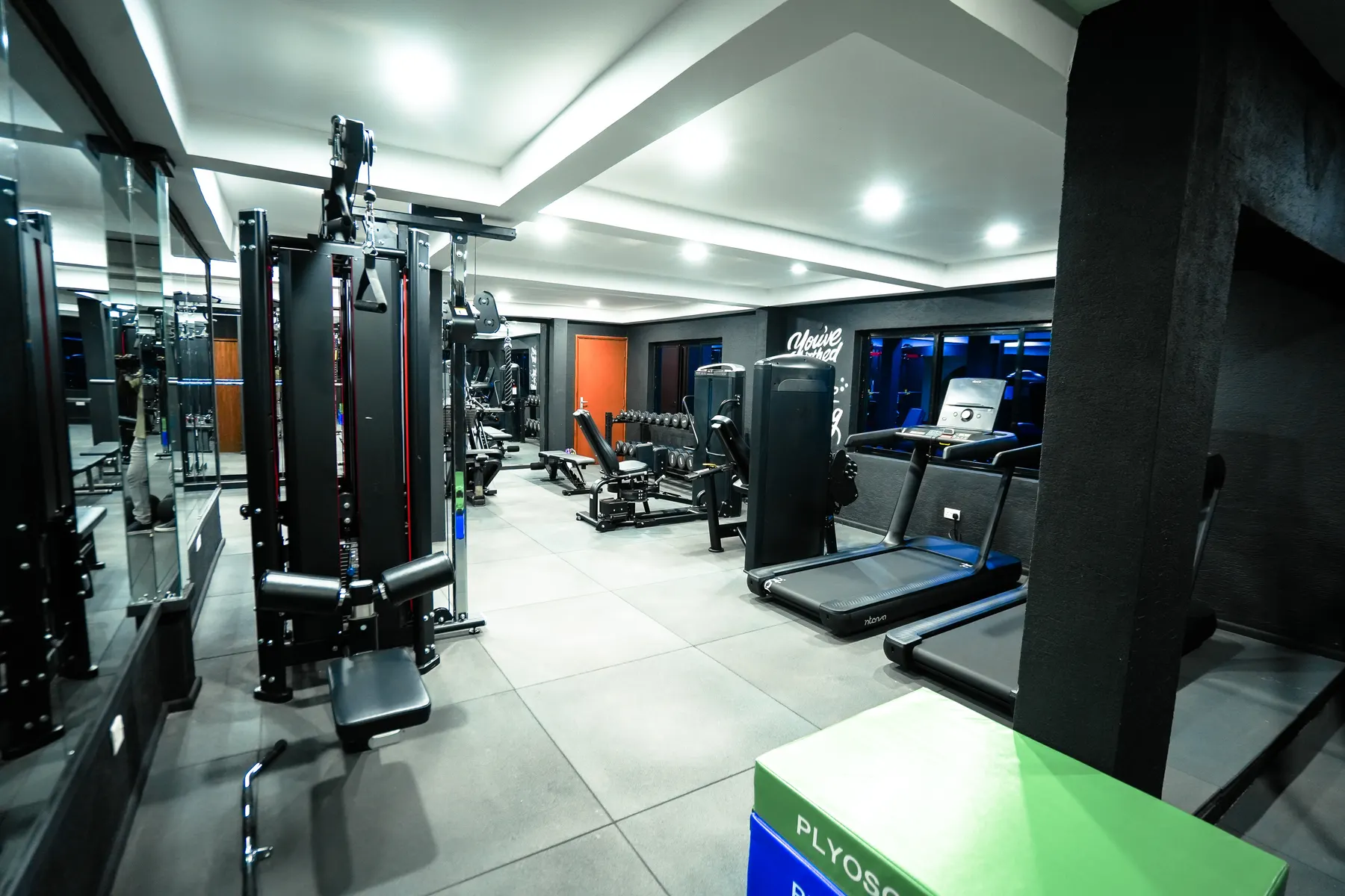 Strength machines and treadmills along the mirrored wall of the gym